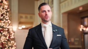 Man in a formal suit speaking at a WEHBA event with a festive Christmas tree in the background, reflecting ROC Media's partnership with the West End Home Builders’ Association.