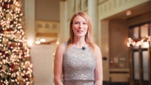 Woman in a sparkling silver dress speaking in a festive venue with a Christmas tree, representing WEHBA events and ROC Media's video production services.