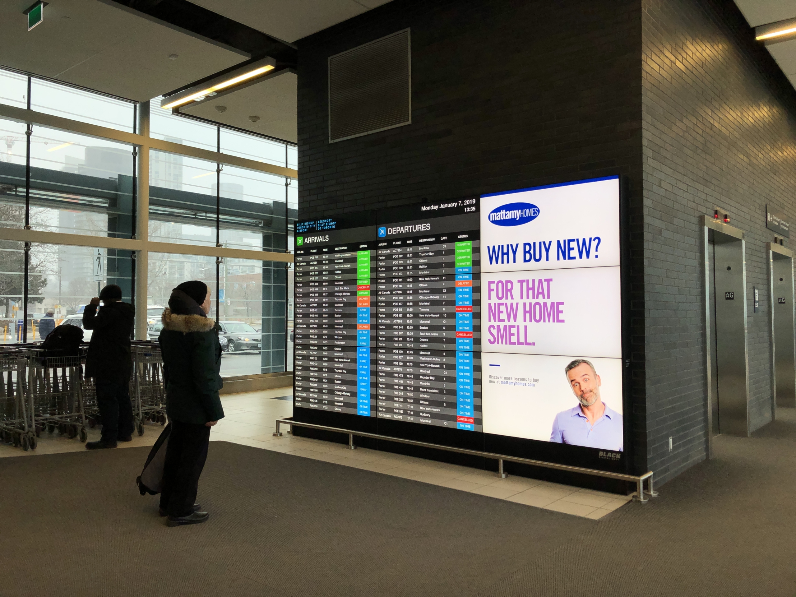 Person looking at digital display board featuring Mattamy Homes advertisement with the text "Why Buy New? For That New Home Smell." in a public space.