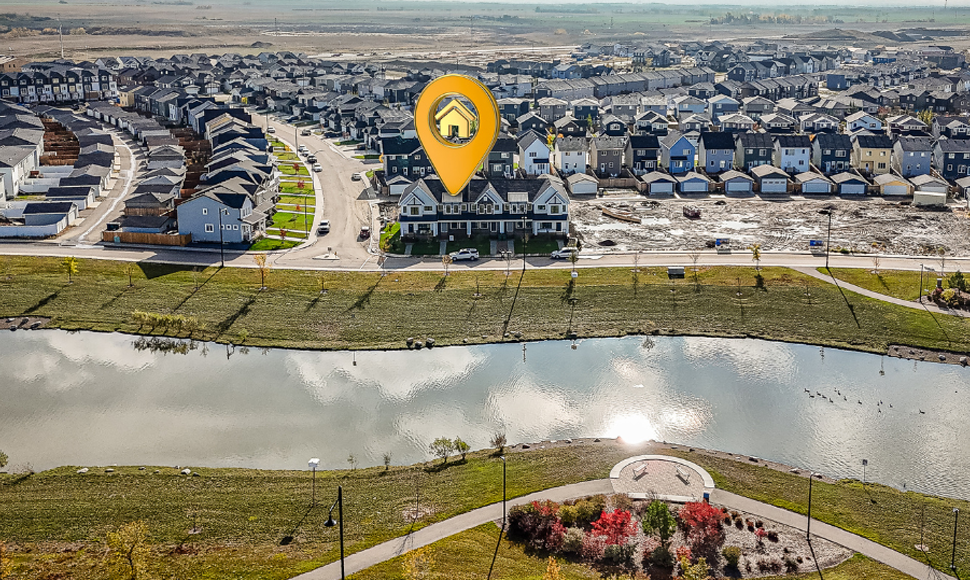 Aerial view of a residential area featuring a highlighted home with a location pin, surrounded by a pond and landscaped green space, representing land development and homebuilding marketing strategies.