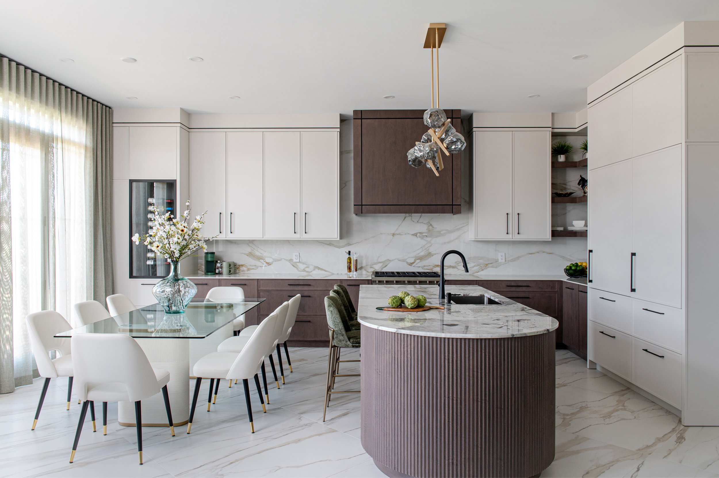 Modern kitchen featuring sleek cabinetry, a glass dining table with white chairs, a decorative vase with flowers, and a stylish island with marble countertops, reflecting contemporary design trends in real estate.