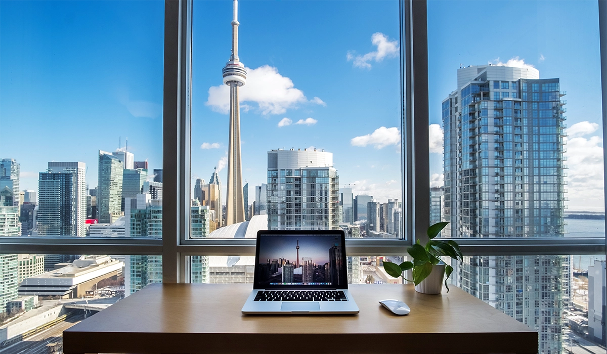 Modern workspace with laptop showcasing Toronto skyline, including CN Tower, and a green plant on wooden desk, emphasizing digital marketing and business growth.