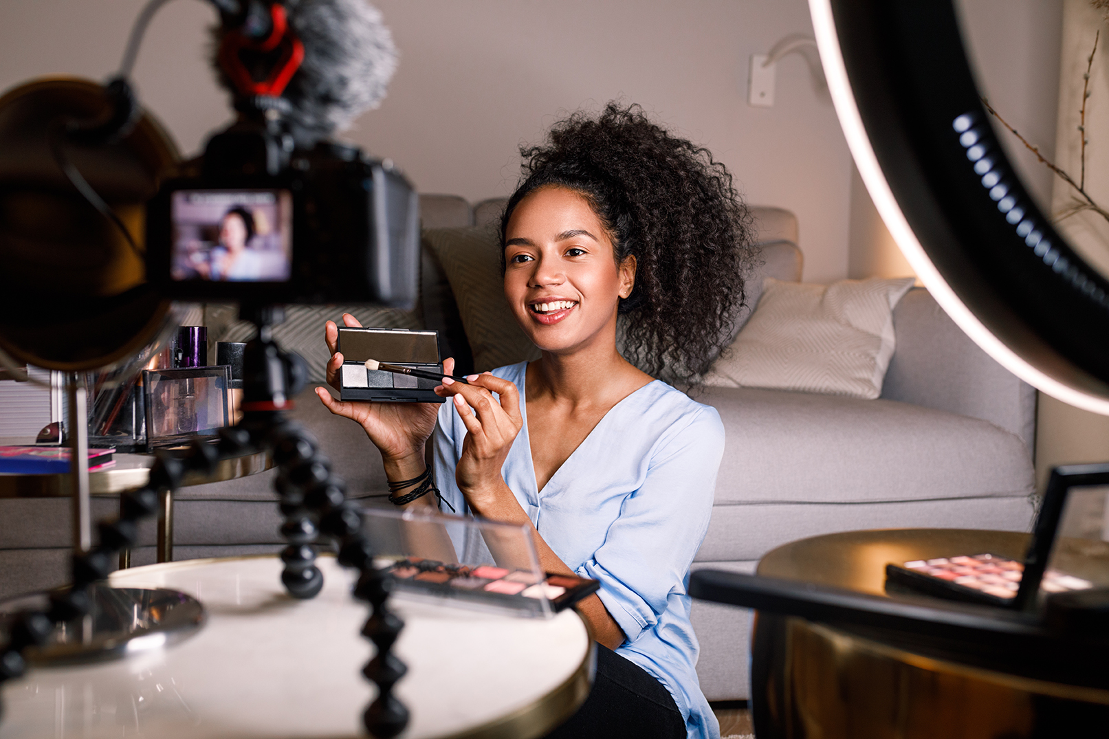 Content creator demonstrating makeup application while filming with a camera, surrounded by beauty products and a ring light, highlighting influencer marketing and engagement strategies.