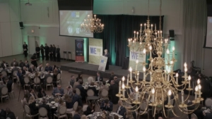 Awards Gala event setting with attendees at tables, chandelier lighting, and a speaker presenting on stage, reflecting the WEHBA community spirit and ROC Media's videography work.